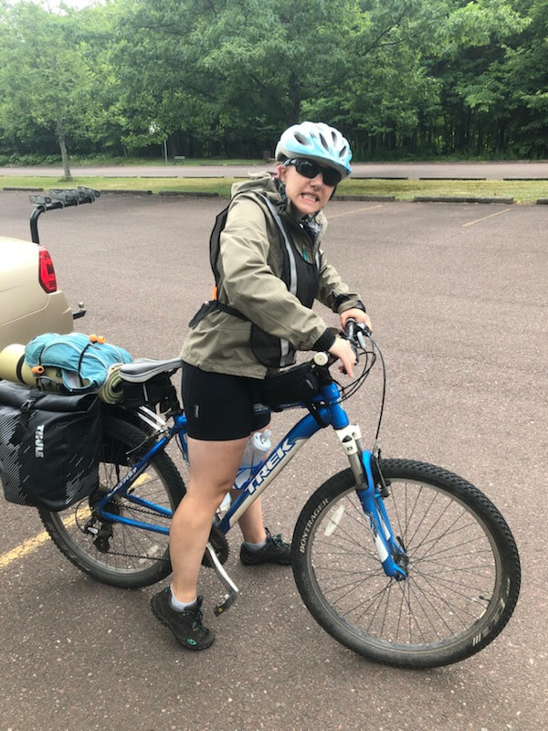 eryn grimacing at the camera while straddling her mountain bike with two full rear panniers in a parking lot
